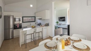 A modern kitchen with white cabinetry, a stainless steel refrigerator, a built-in oven, and a microwave. There is a dining area with a table set for two, including plates, glasses, and a jug of juice. - Playa Blanca Beach Mate (Yaiza)