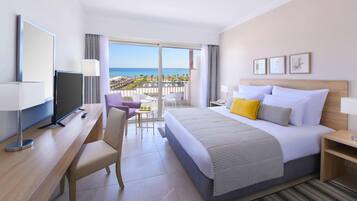 Habitación de hotel con cama, escritorio, televisor, balcón con vista a la playa y ventana.