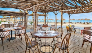 A beachside restaurant with outdoor seating, tables, and chairs, overlooking the beach and ocean.