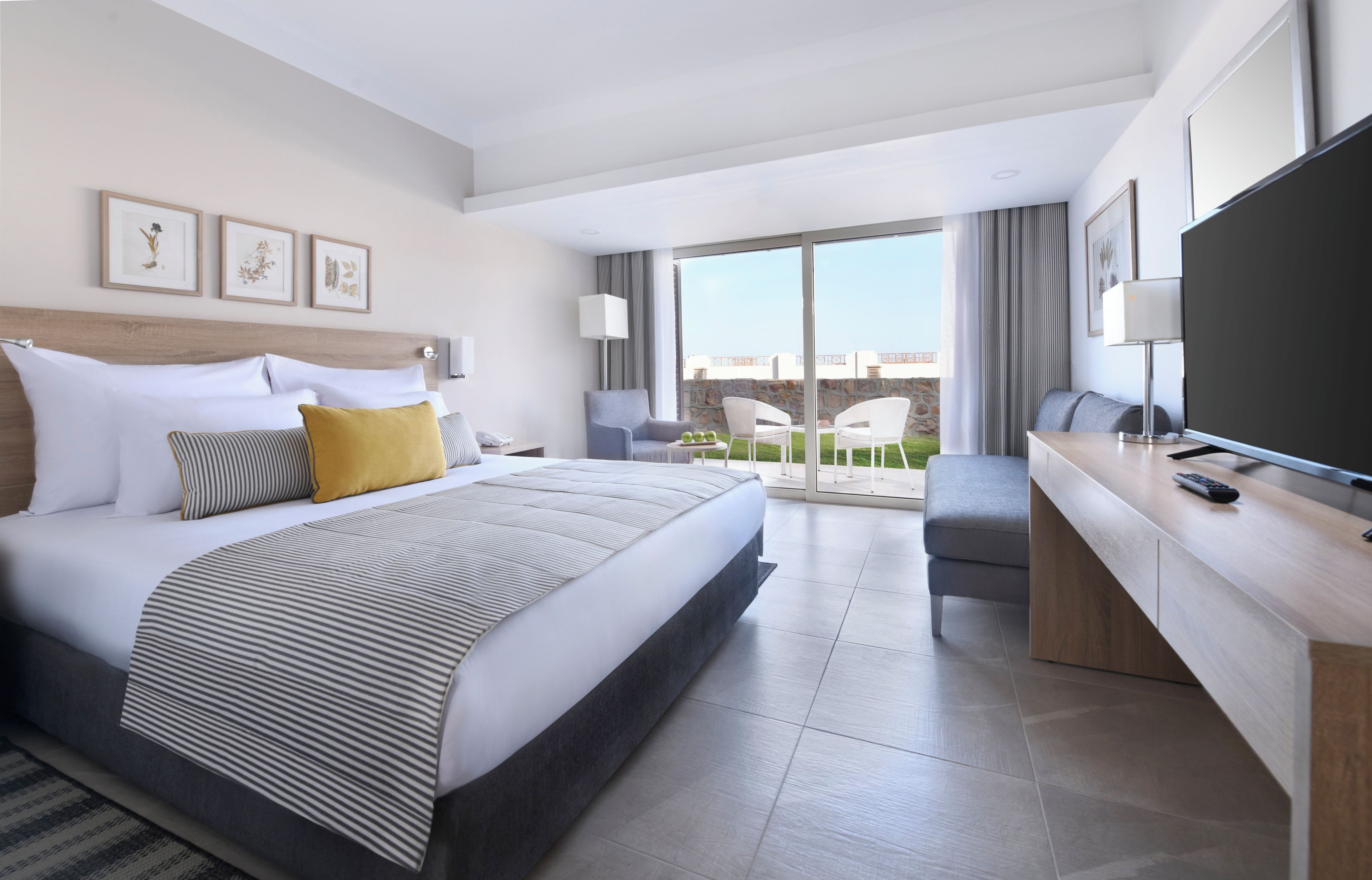 Quarto de hotel moderno com uma cama grande, uma escrivaninha, televisão e varanda com vista.