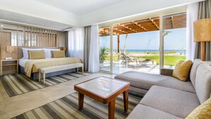 A hotel room with a bed, a sofa, a coffee table, and a view of the beach.