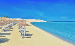 Una playa con filas de tumbonas y sombrillas, cielo azul despejado y mar tranquilo.