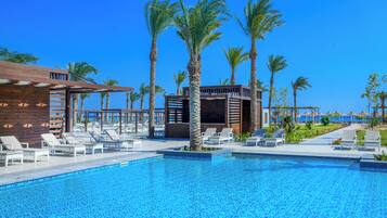 Zona de piscina con sillones, palmeras y una estructura de edificio de madera.