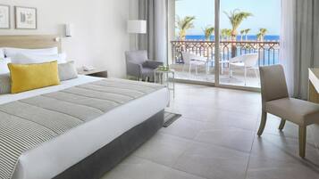 A hotel room with a bed, a desk, a chair, a balcony with a view of the beach and ocean.
