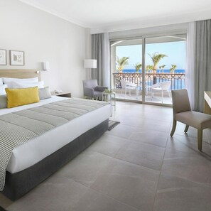 Habitación de hotel con cama, escritorio, silla y balcón con vista a la playa y al océano.