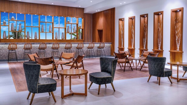 Un lobby moderno con paneles de madera, un ventanal con jarrones y arreglos de asientos.