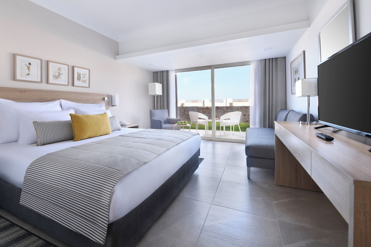 Une chambre d’hôtel moderne dotée d’un grand lit, d’un bureau, d’une télévision à écran plat et d’un balcon avec vue.