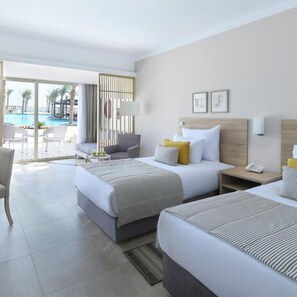 A hotel room with two beds, a sofa, a small table, and a view of a swimming pool.