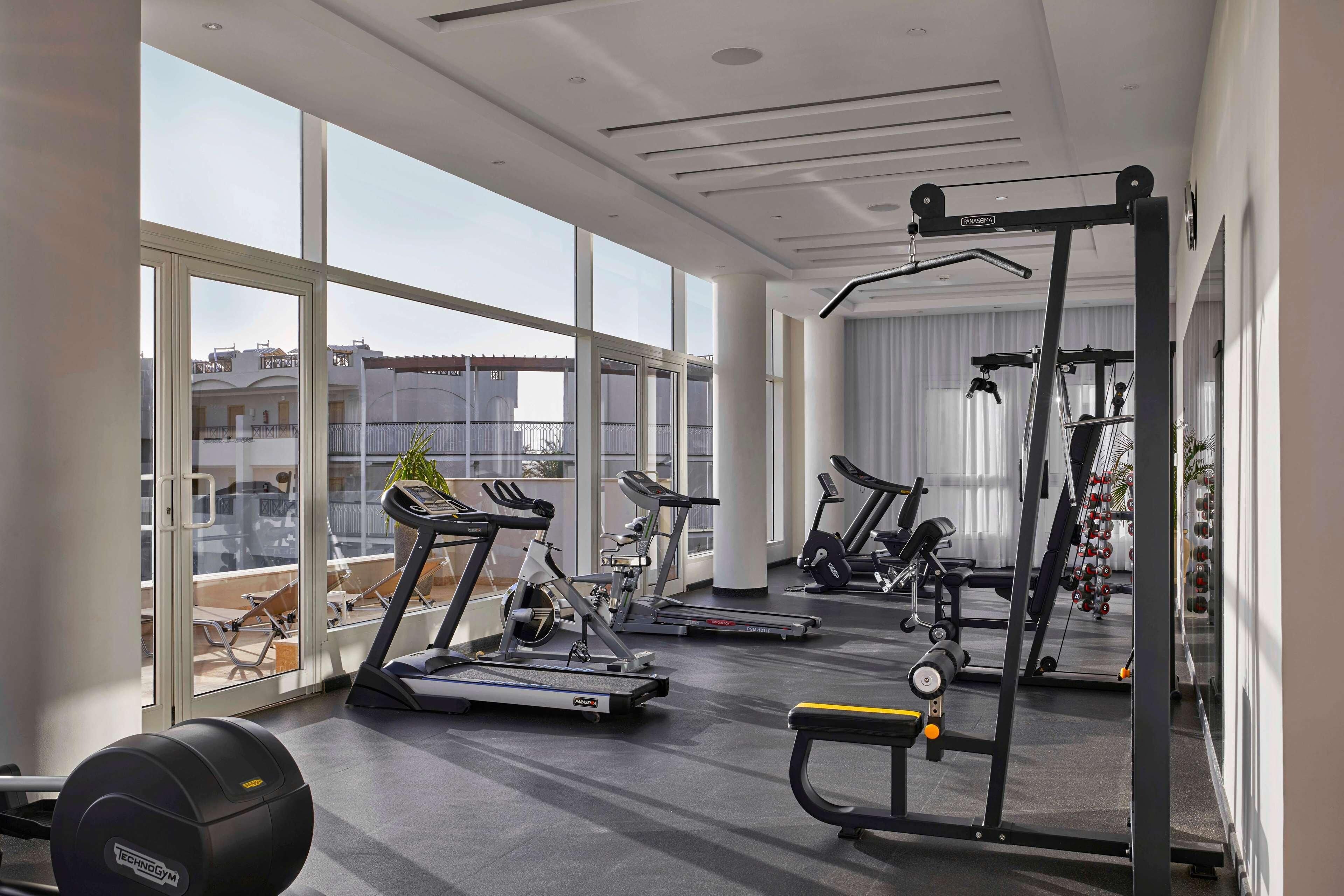 A modern gym with cardio machines, free weights, and a mirror.