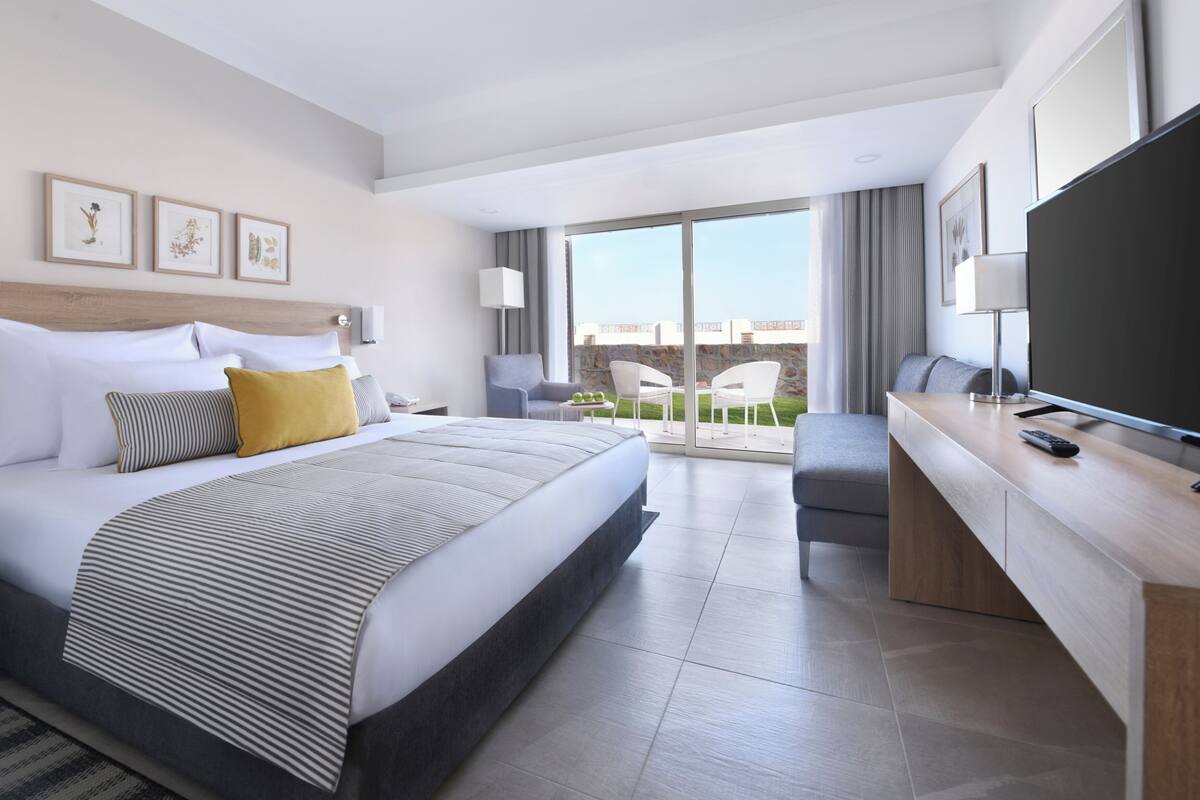 A modern hotel room with a large bed, a desk, a flat-screen TV, and a balcony with a view.