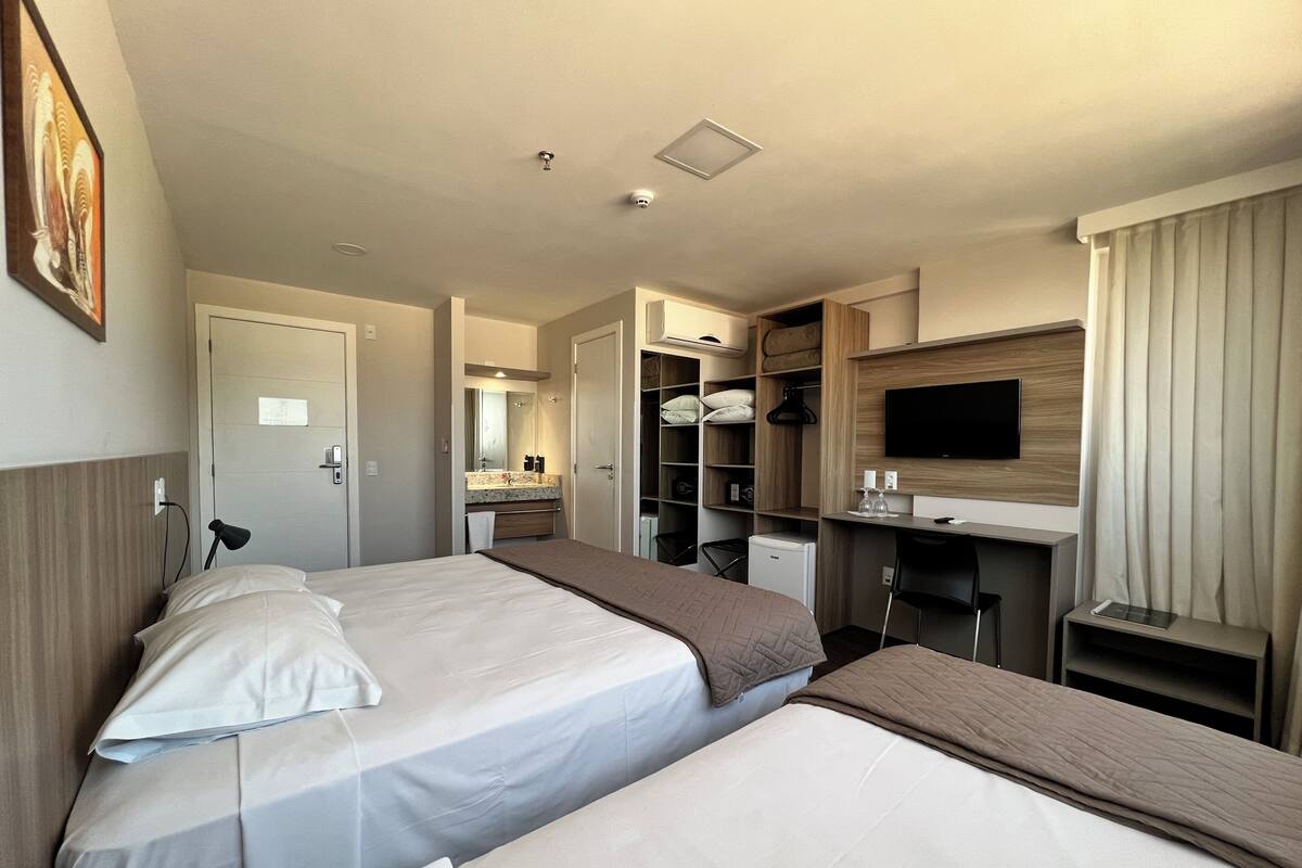 A hotel room with two beds, a TV, a desk, and a wardrobe.