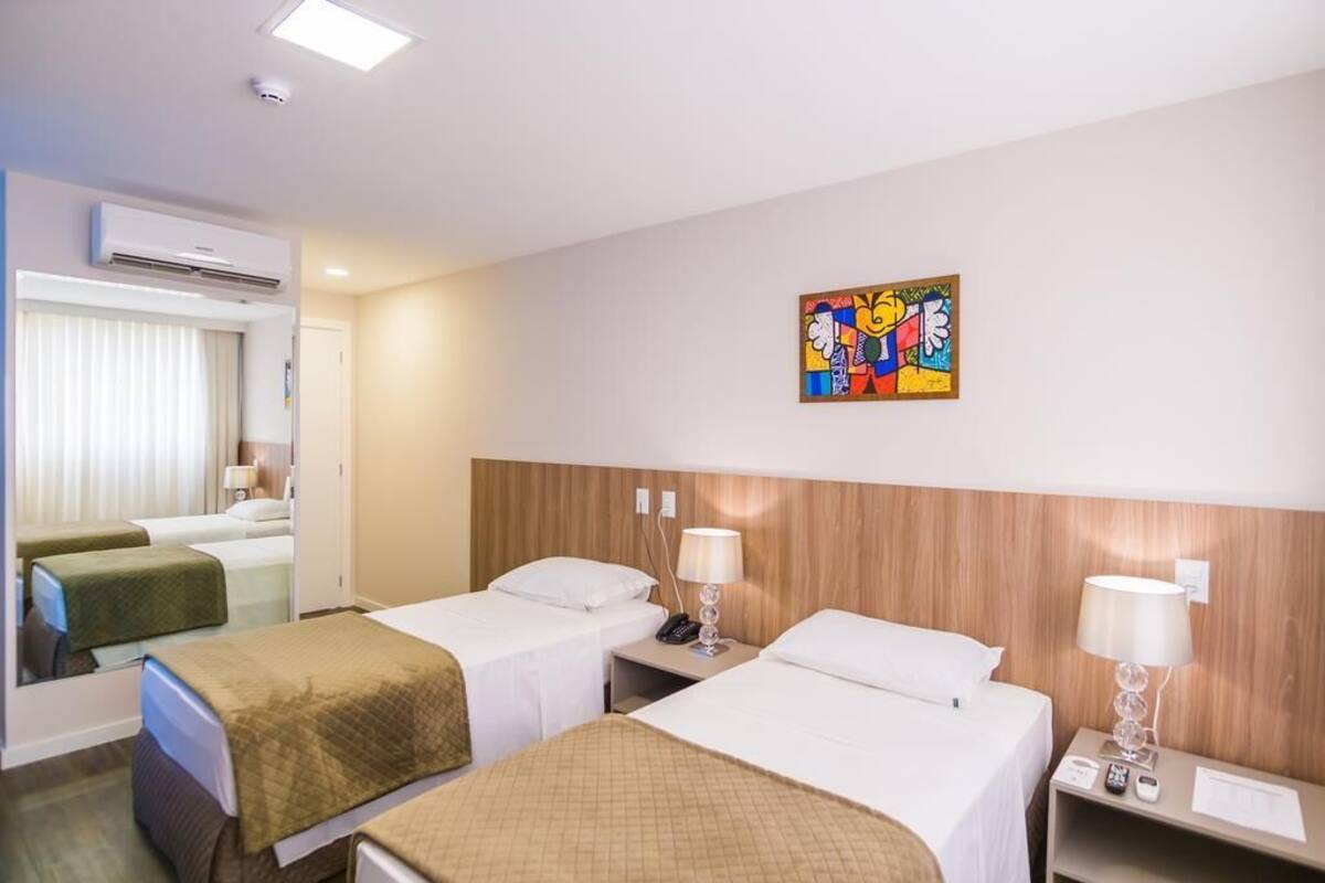 A hotel room with two beds, a wooden headboard, a wall-mounted artwork, and a mirror.