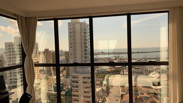 A room with a large window offering a view of a cityscape and a body of water. - Hotel 7 Itajai (Itajai)