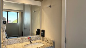 Une salle de bain dotée d’un lavabo avec un plan de toilette en granit, d’un miroir, d’un sèche-cheveux et offrant une vue sur l’extérieur par la fenêtre.