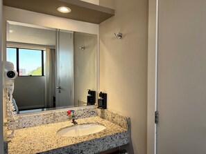 A bathroom with a granite countertop sink, a mirror, a hairdryer, and a view of the outside through the window. - Hotel 7 Itajai (Itajai)