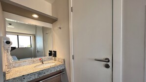 Un baño con lavamanos de encimera de granito, un espejo, toallero, cubo de basura y una puerta con manija.