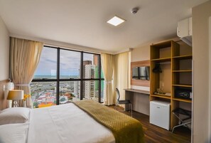 A hotel room with a bed, a desk, a chair, a TV, and a view of the city. - Hotel 7 Itajai (Itajai)