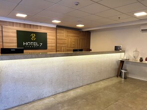 A hotel reception desk with a digital display, a wooden panel wall, and a tiled floor. - Hotel 7 Itajai (Itajai)