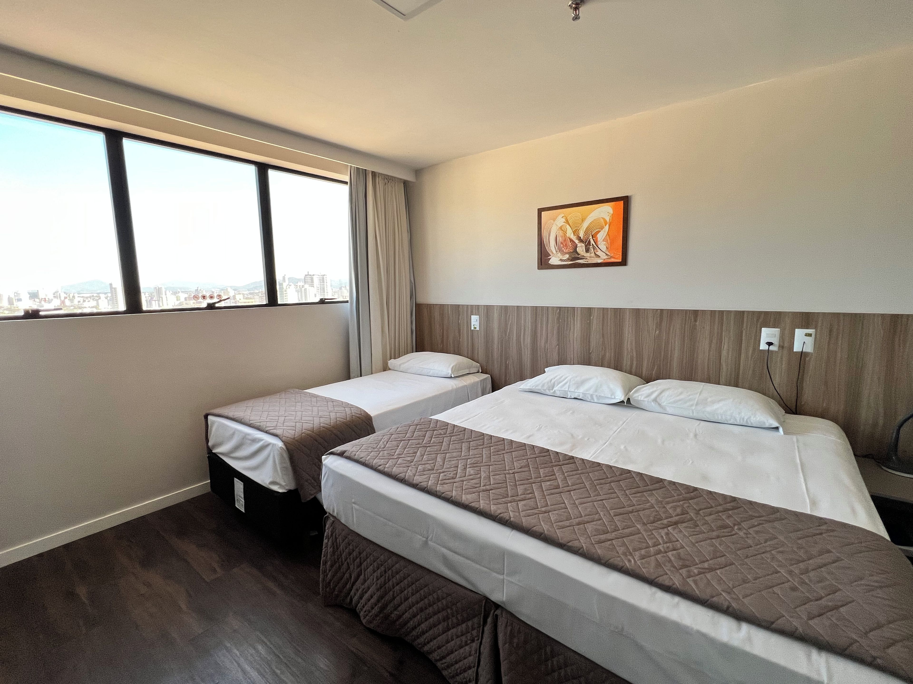 A hotel room with two beds, a city view, a painting on the wall, and a wooden headboard.