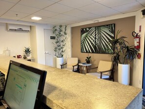 A reception area with a computer monitor, chairs, potted plants, and a large wall painting. - Hotel 7 Itajai (Itajai)