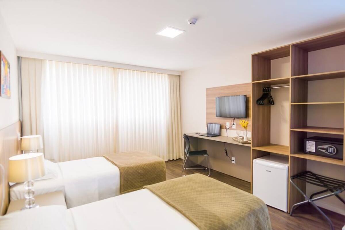 A hotel room with two beds, a desk, a chair, a TV, a mini-fridge, and a wardrobe.