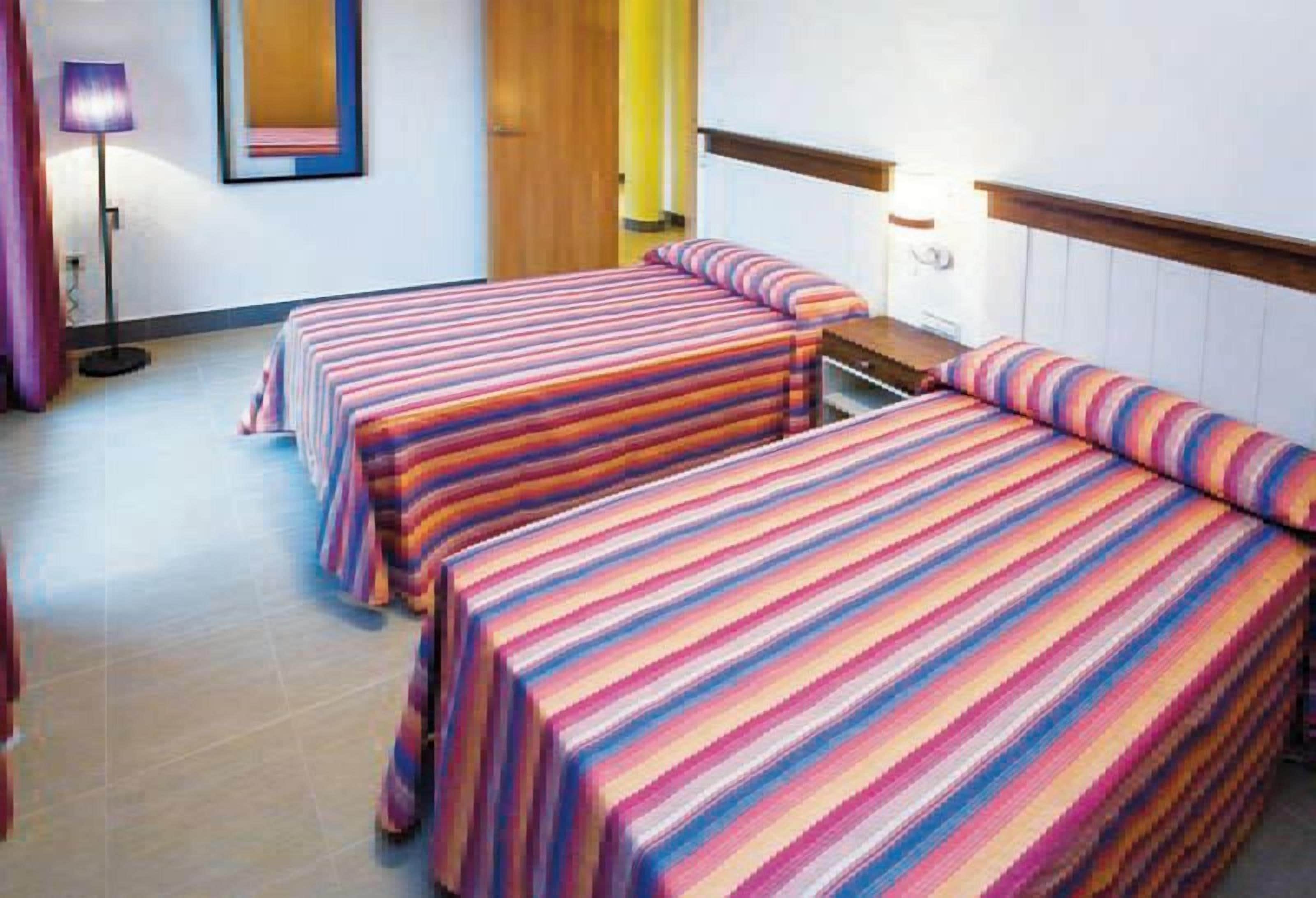 Una habitación de hotel con dos camas, una mesita de noche, una lámpara y un espejo en la pared.