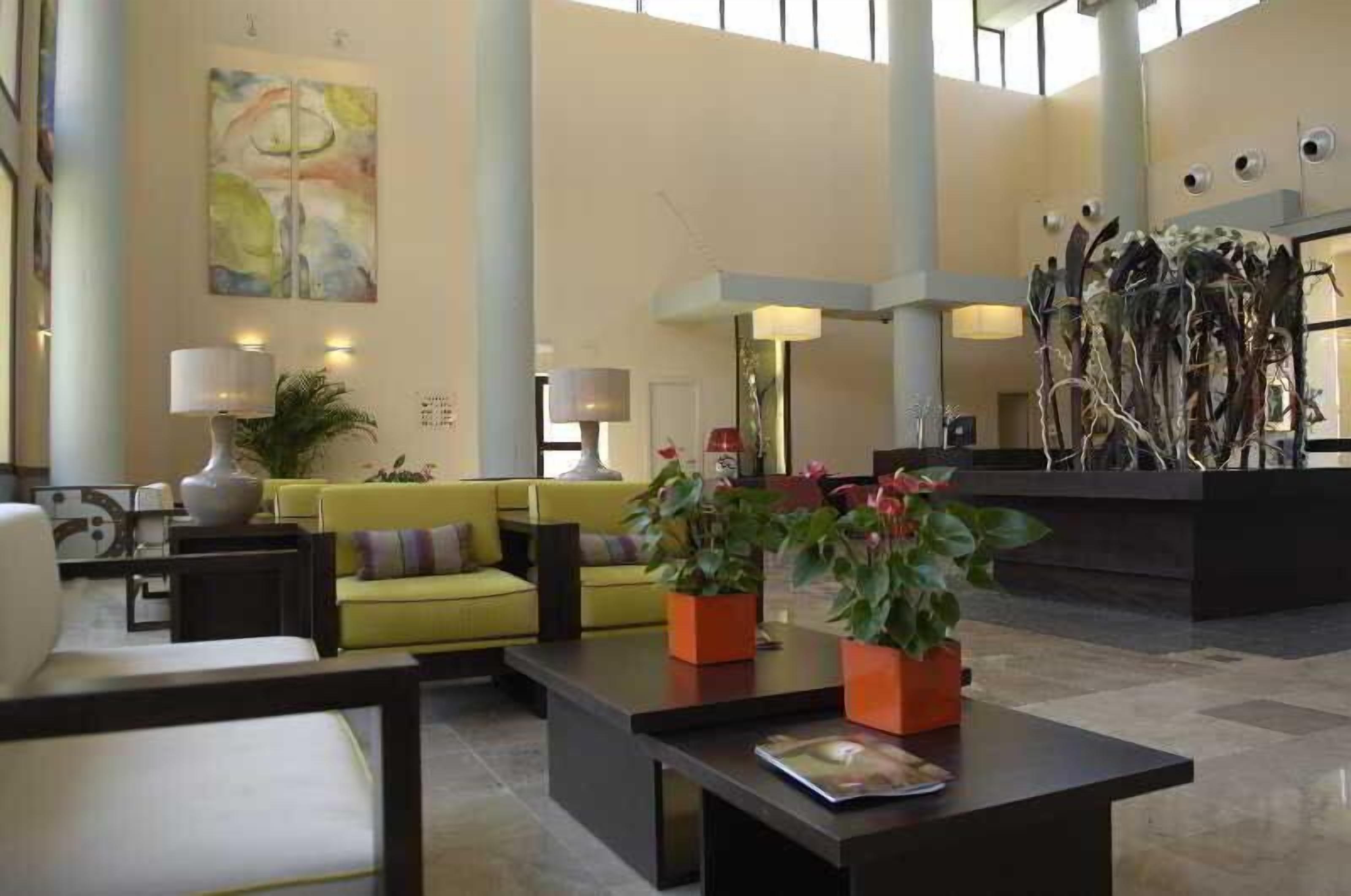 A spacious lobby with a yellow sofa, a black reception desk, and potted plants.