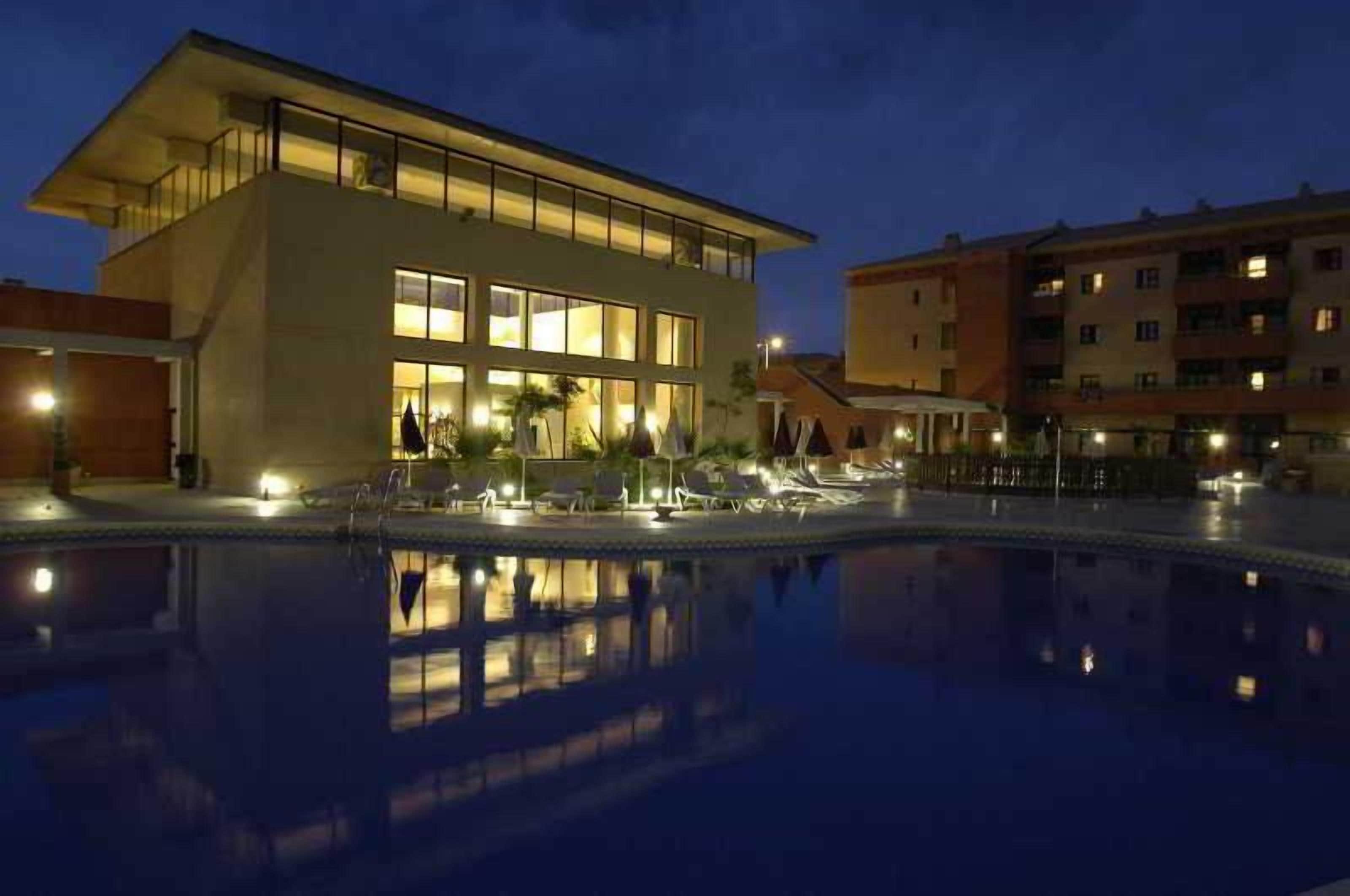 A modern hotel with a pool, reflecting the building and surroundings.