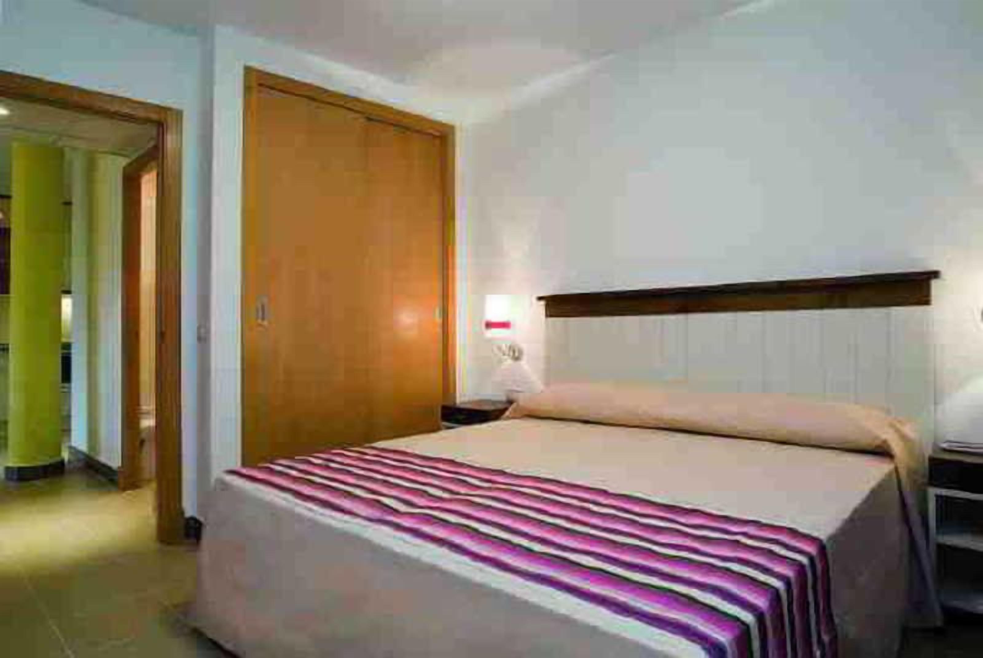 Habitació d'hotel amb un llit, una porta de fusta i una taula de nit.