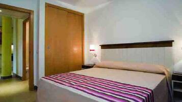 Habitació d'hotel amb un llit, una porta de fusta i una taula de nit.