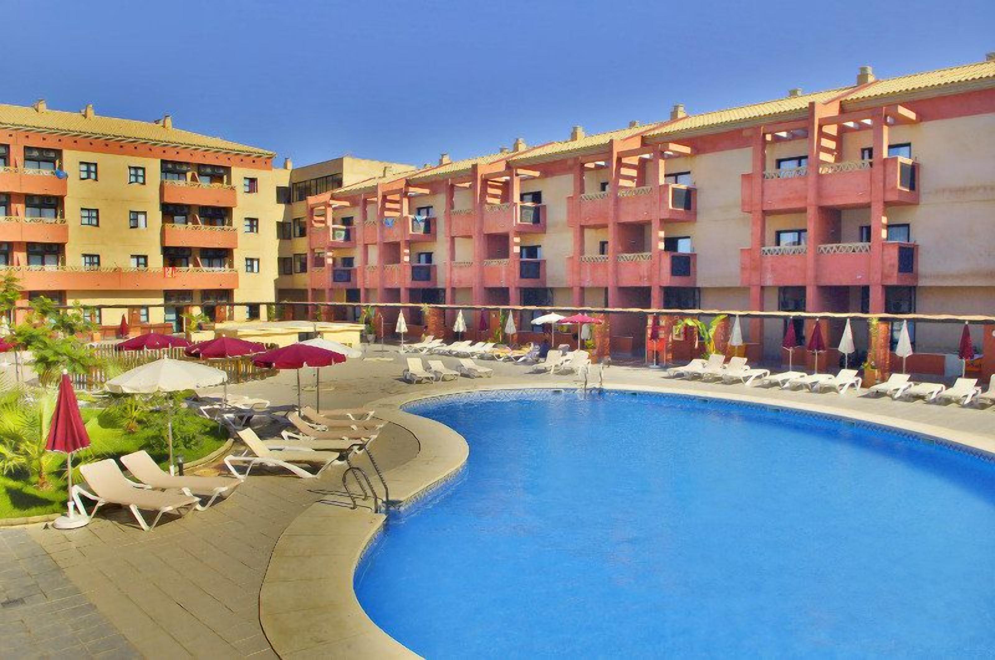 Ett hotell med en swimmingpool, solstolar och parasoller.