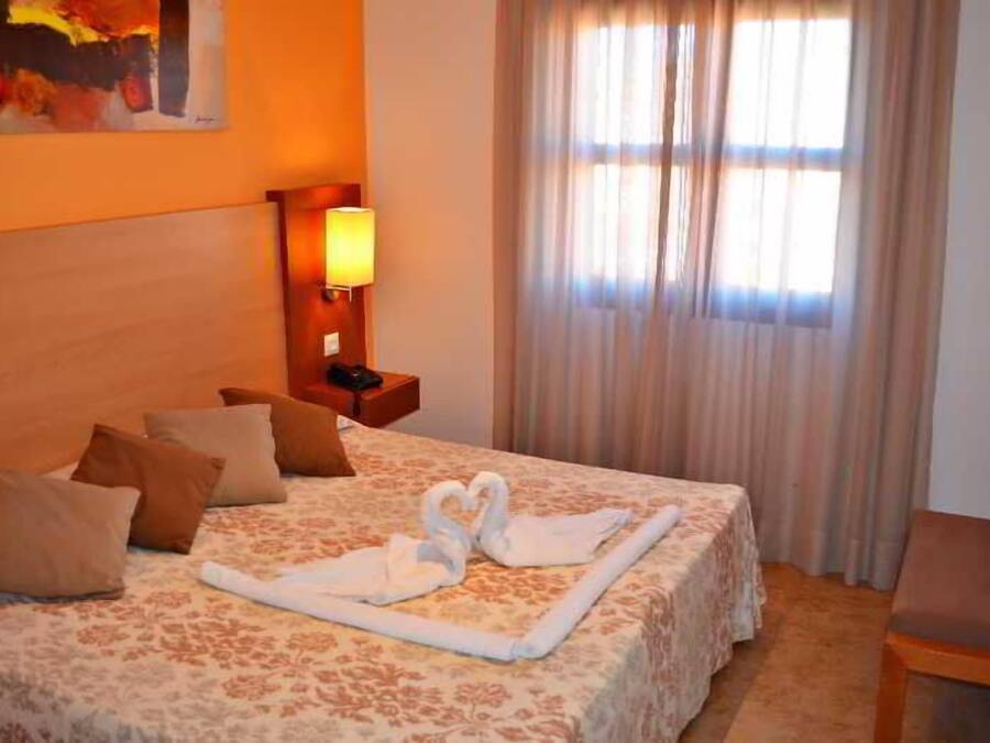 A hotel room with a bed, pillows, a bedside lamp, a chair, and a window with curtains.