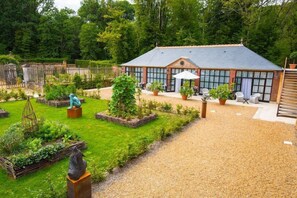 A brick building with large windows, a patio with outdoor seating, and a garden with various plants and sculptures. - Relais DU Silence Domaine DE LA Groirie Hotel AND Seminars (Trange)
