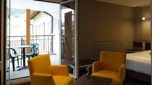A hotel room with a bed, two yellow armchairs, a small table, and a glass door leading to an outdoor area with a table and chairs. - Hotel Les Bergeronnettes (Champagneux)