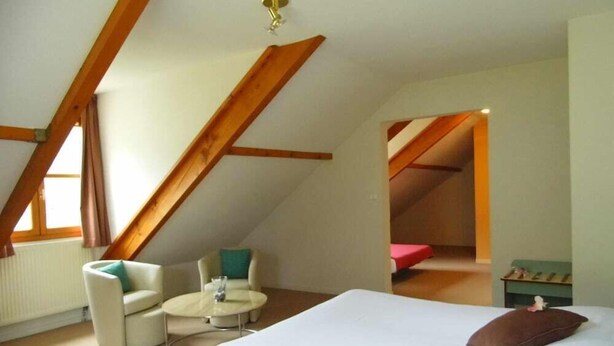 A bedroom with a bed, a chair, a small table, and a window. - Hotel Les Bergeronnettes (Champagneux)