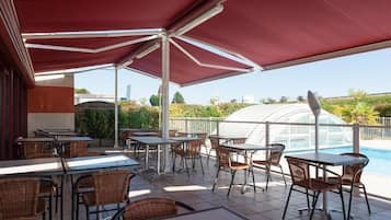 An outdoor patio area with tables and chairs, a swimming pool, and a greenhouse structure.