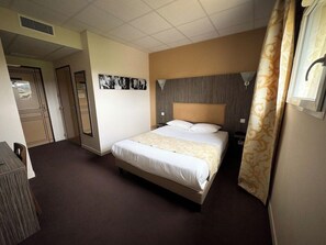 Habitación de hotel con cama, escritorio, espejo y un cuadro colgado en la pared.