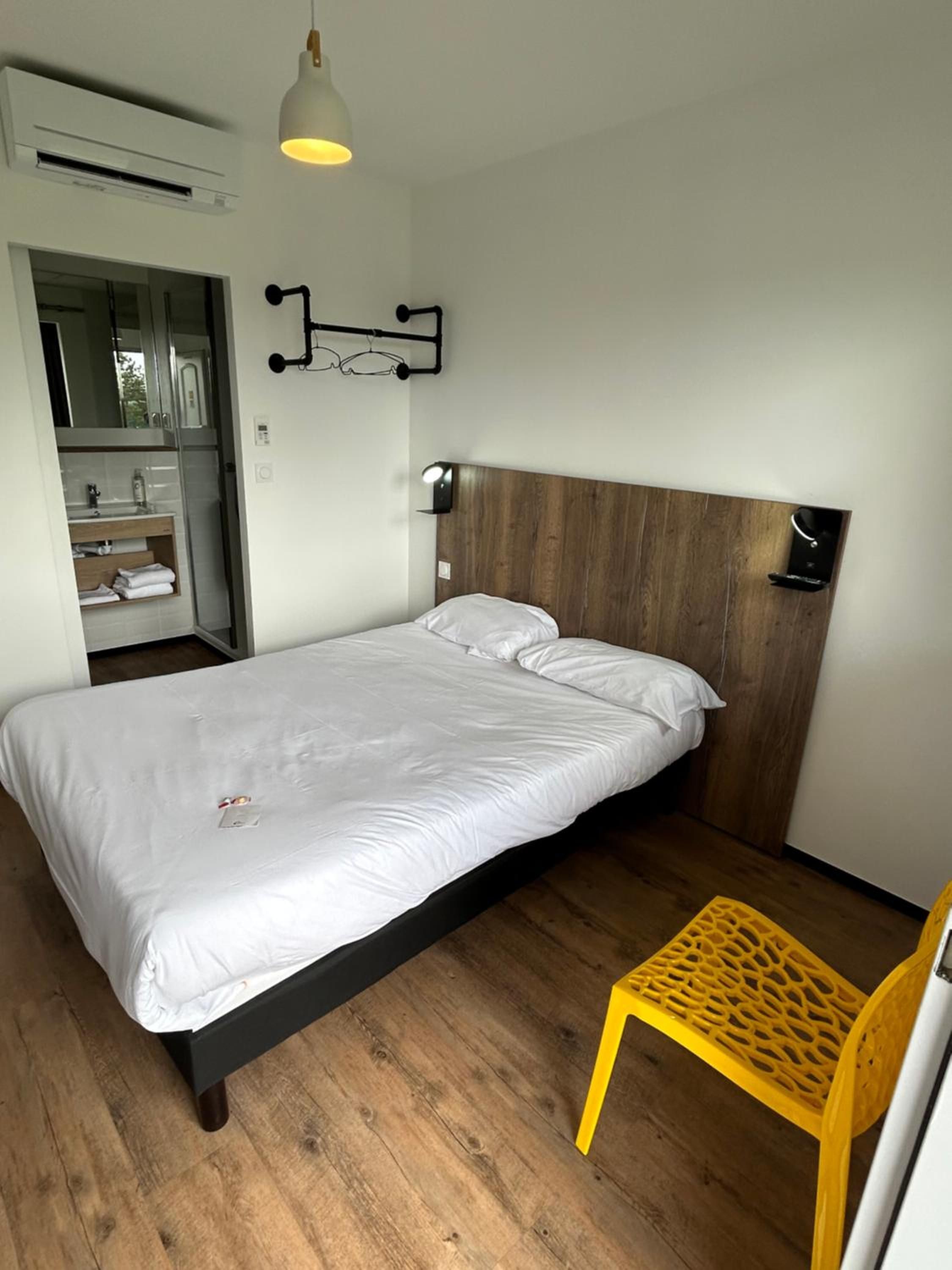 A bedroom with a bed, a wooden headboard, a bedside table, a mirror, and a yellow chair.