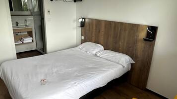 A bedroom with a bed, a wooden headboard, a bedside table, a mirror, and a yellow chair.