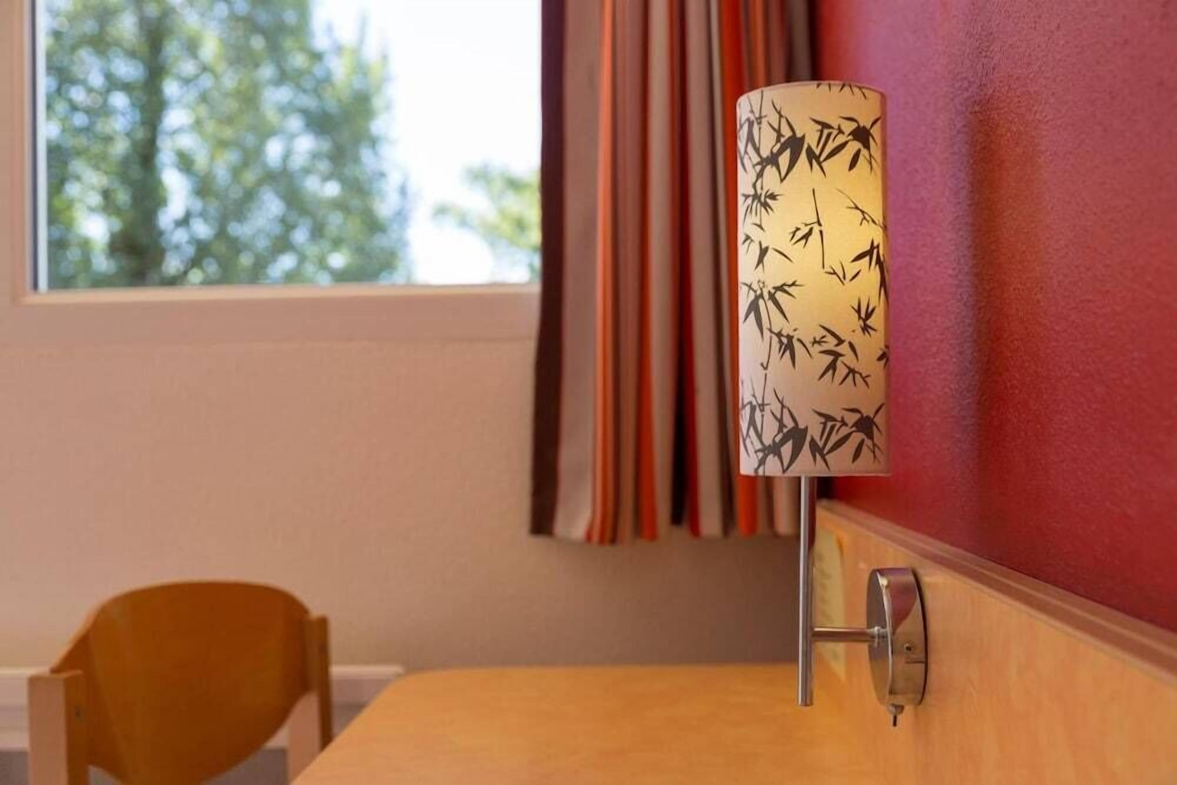 Une lampe ornée d’un motif en bambou sur un mur, une chaise en bois et une fenêtre avec des rideaux.