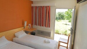 Camera d'albergo con due letti, un tavolino, una televisione e una finestra con tende.