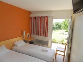 Quarto de hotel com duas camas, uma mesinha, uma televisão e uma janela com cortinas.