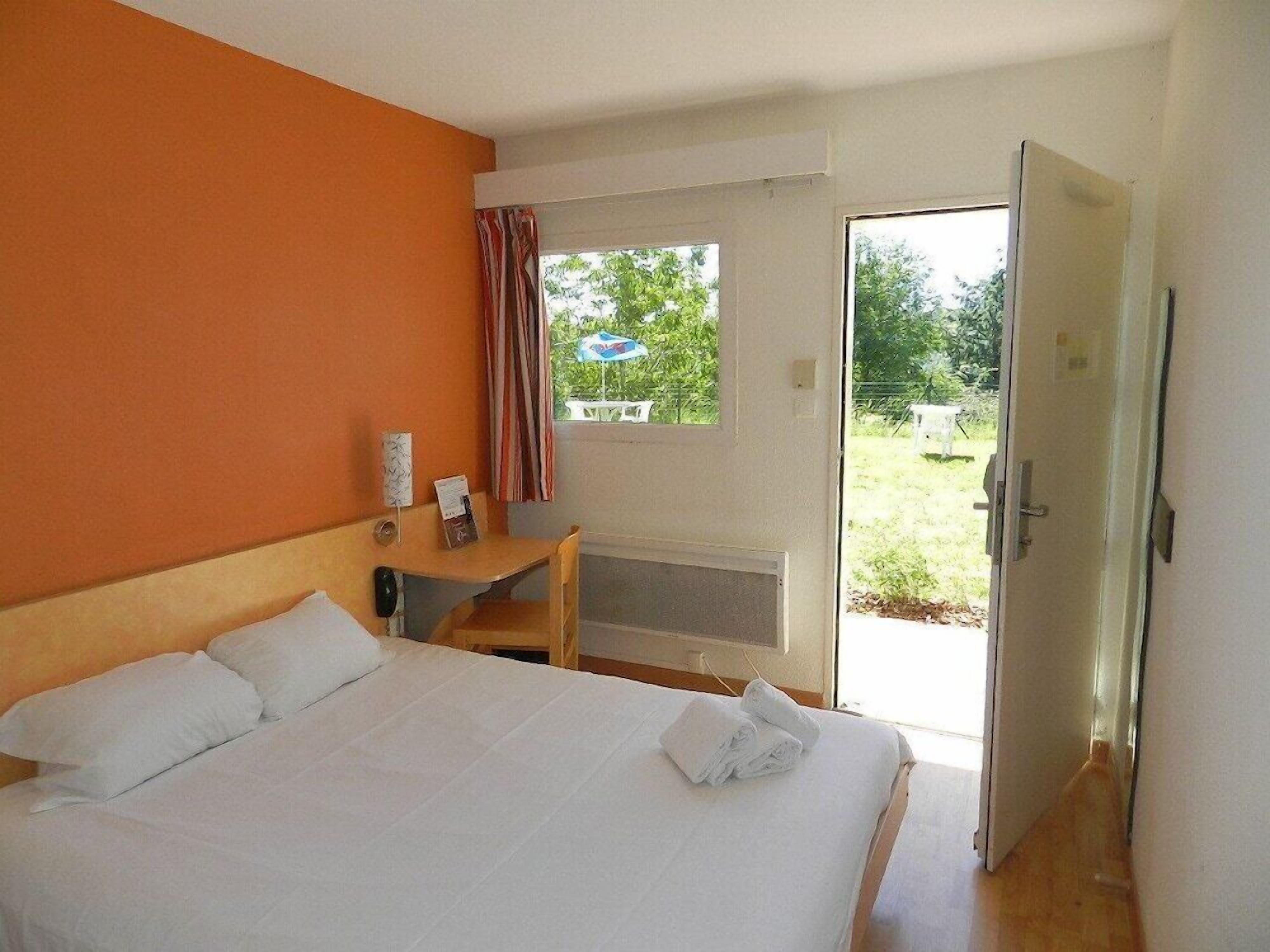 Habitación de hotel con cama, escritorio y ventana con cortinas.