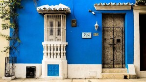 Ein Gebäude mit blauer Fassade, einem weißen Balkon mit filigraner Balustrade, einer schwarzen schmiedeeisernen Tür und einem kleinen Schild mit der Nummer 9-73.