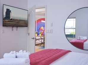 Un dormitorio con cama, un espejo grande, un cuadro y vistas a través de una puerta abierta.