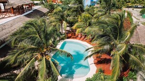 A resort with a central swimming pool surrounded by palm trees, outdoor seating, and thatched-roof structures. - Ensueno Holbox & Beach Club (Isla Holbox)