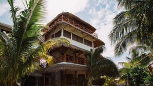 A two-story building with a thatched roof and wooden balcony railings, surrounded by palm trees. - Ensueno Holbox & Beach Club (Isla Holbox)
