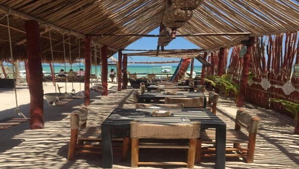 An outdoor dining area with thatched roof, wooden tables, and chairs, overlooking a beach. - Ensueno Holbox & Beach Club (Isla Holbox)