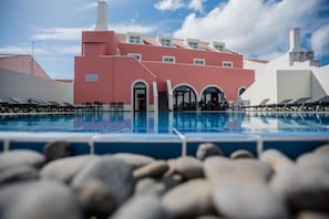 Una piscina con sillas de descanso, un edificio de fachada roja y un cielo despejado.