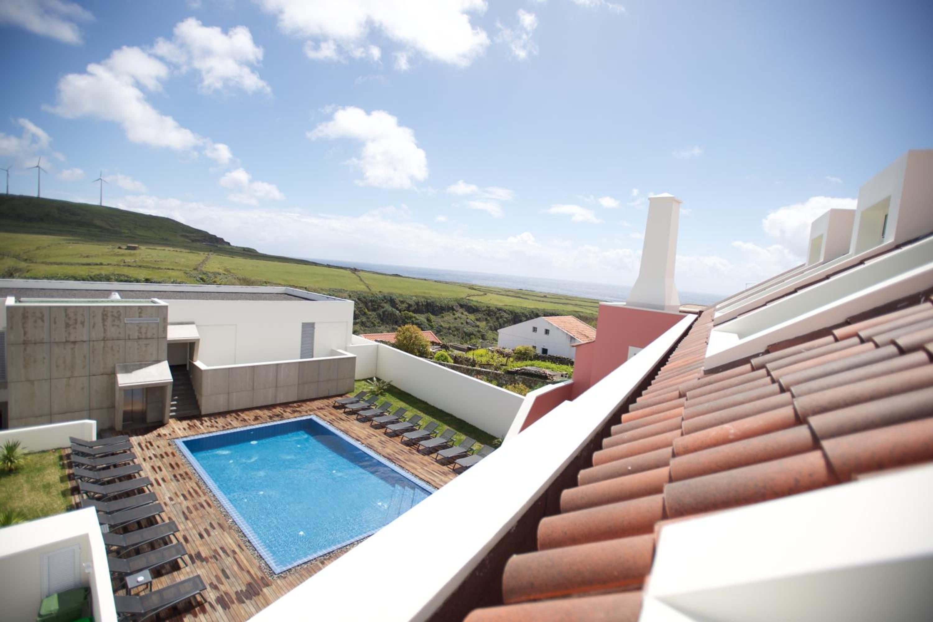 A rooftop pool with a view of the sea and wind turbines in the distance.